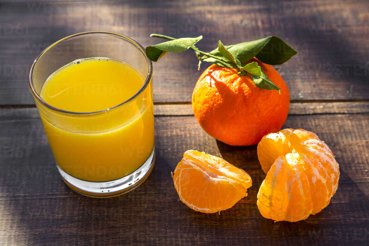 Orangen und ein Glas frischer Orangesaft auf braunen Holz-…