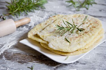 Stack of naan breads with rosemary twig on plate - YFF000509
