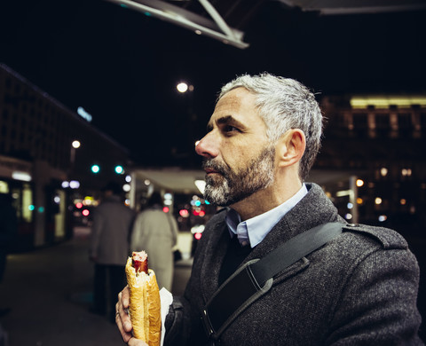 Österreich, Wien, Mann mit Käsekrainerwurst bei Nacht, lizenzfreies Stockfoto