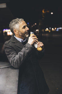 Austria, Vienna, man with Cheese Carniolan sausage at sausage booth by night - AIF000209