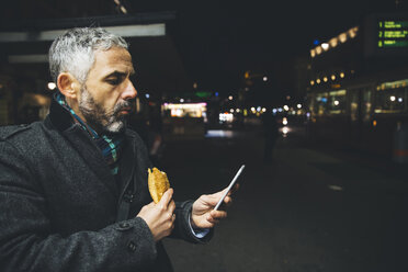 Österreich, Wien, Mann mit Käsekrainerwurst schaut bei Nacht auf sein Smartphone - AIF000212