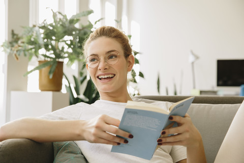 Junge Frau zu Hause, schaut von ihrem Buch auf und lacht, lizenzfreies Stockfoto