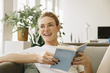 Young woman at home, looking up from her book, laughing - MFF002577