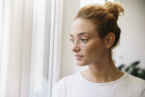 Junge Frau mit Brille schaut aus dem Fenster, lizenzfreies Stockfoto