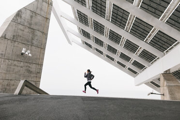 Spain, Barcelona, jogging woman under solar plant - EBSF001210