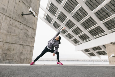 Spain, Barcelona, female jogger, stretching excersice under solar plant - EBSF001211