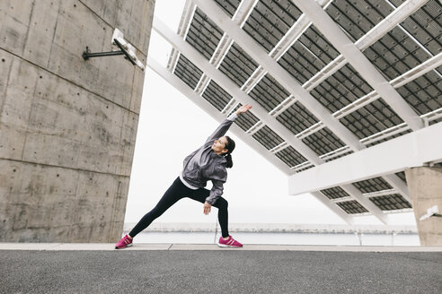 Spain, Barcelona, female jogger, stretching excersice under solar plant - EBSF001211