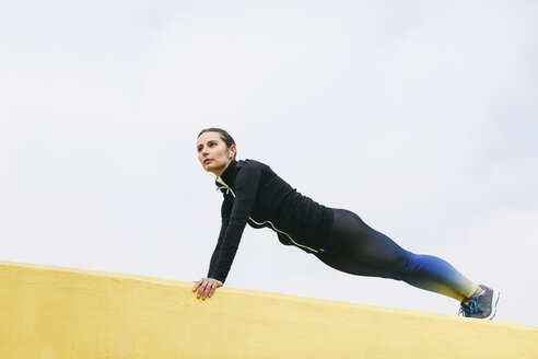 Spain, Barcelona, female jogger on yellow wall, pushup - EBSF001220