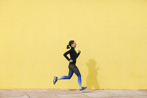 Spain, Barcelona, jogging woman in front of yellow wall - EBSF001222