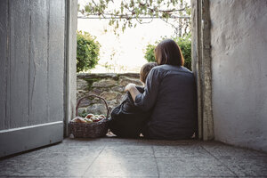 Spanien, Asturien, Rückenansicht von Mutter und Sohn, die am Eingang eines Landhauses sitzen - DAPF000004