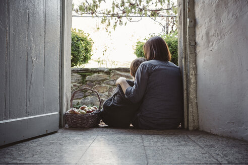 Spain, Asturias, back view of mother and son sitting at entrance of country house - DAPF000004