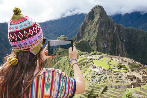 Peru, woman taking pictures of Machu Picchu citadel and Huayna Picchu mountain with a tablet - GEMF000626