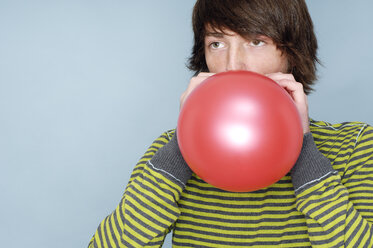 Teenage boy blowing red balloon in front of blue background - GUFF000183