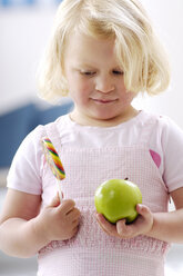 Portrait of little blond girl holding a green apple and a lollipop - GUFF000201