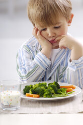 Portrait of little blond boy looking at plate with vegetables - GUFF000204