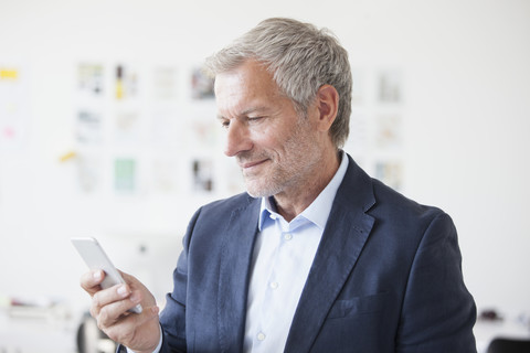 Geschäftsmann im Büro schaut auf sein Handy, lizenzfreies Stockfoto