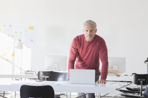 Portrait of confident businessman with laptop in office stock photo