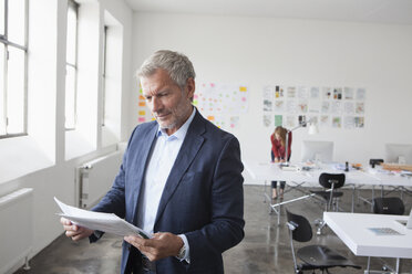 Geschäftsmann im Büro schaut auf Papier - RBF004017