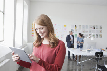 Lächelnde junge Frau, die ein digitales Tablet im Büro benutzt - RBF004022