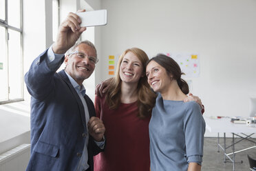 Ein lächelnder Geschäftsmann macht ein Selfie mit zwei Frauen im Büro - RBF004024