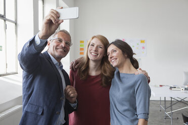 Smiling businessman taking a selfie with two women in office - RBF004024