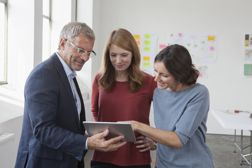 Lächelnder Angestellter und zwei Frauen im Büro, die auf ein digitales Tablet schauen - RBF004025