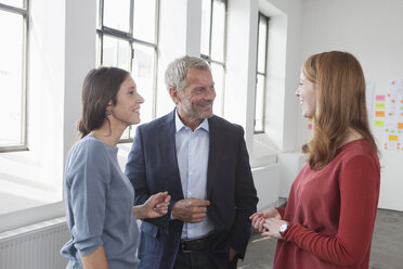 Lächelnder Geschäftsmann und zwei Frauen im Büro im Gespräch - RBF004027