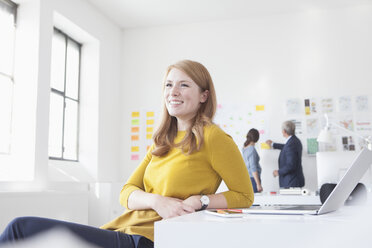 Lächelnde junge Frau im Büro am Schreibtisch - RBF004048