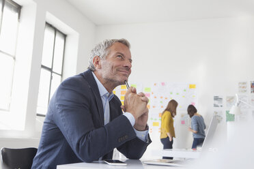 Smiling businessman in office at desk thinking - RBF004053