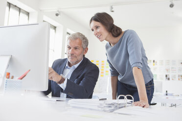 Businessman and woman in office working on computer together - RBF004058