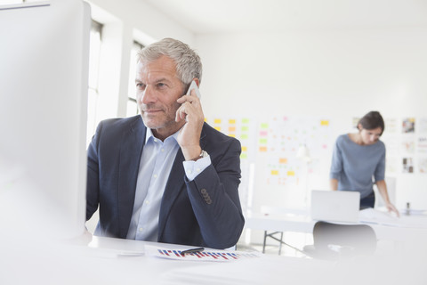 Geschäftsmann im Büro am Schreibtisch am Mobiltelefon, lizenzfreies Stockfoto