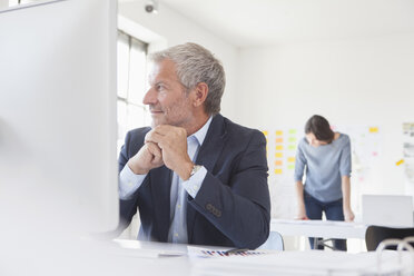 Smiling businessman in office at desk - RBF004062