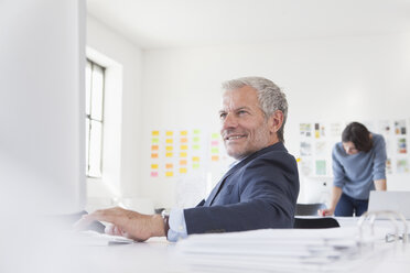 Lächelnder Geschäftsmann im Büro am Schreibtisch - RBF004063