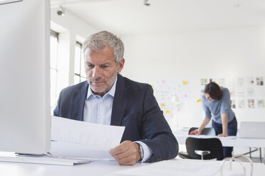 Businessman in office at desk looking at paper - RBF004064