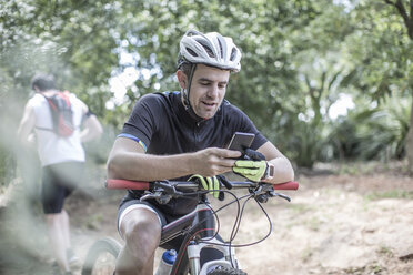 Mann auf Mountainbike im Wald schaut auf sein Handy - ZEF007904