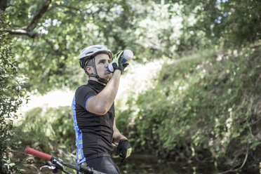 Mann auf Mountainbike im Wald trinkt Wasser - ZEF007909