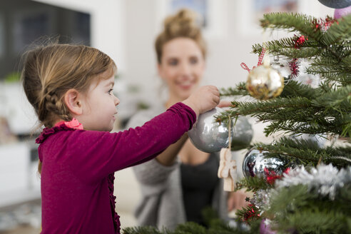 Kleines Mädchen schmückt den Weihnachtsbaum mit ihrer Mutter im Wohnzimmer - SHKF000434