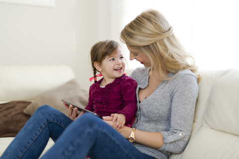 Mother and her little daughter sitting on couch in the living room with digital tablet stock photo