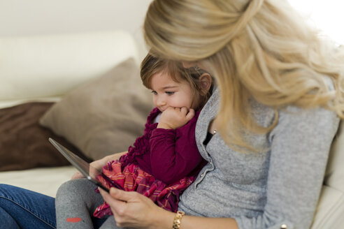 Kleines Mädchen sitzt auf dem Schoß ihrer Mutter und schaut auf ein digitales Tablet - SHKF000439