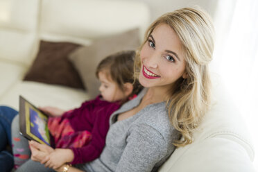 Porträt einer lächelnden Frau, die mit ihrer kleinen Tochter auf der Couch im Wohnzimmer sitzt - SHKF000440