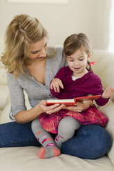 Kleines Mädchen sitzt auf dem Schoß ihrer Mutter und schaut ein Buch an - SHKF000443