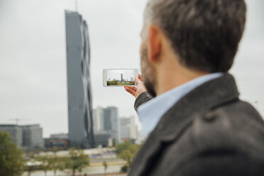 Austria, Vienna, businessman taking a picture of DC Towers with his smartphone - AIF000214