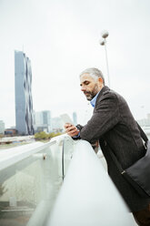 Austria, Vienna, businessman standing on Reichsbruecke looking at his smartphone - AIF000216