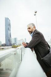Österreich, Wien, Geschäftsmann steht auf der Reichsbrücke und schaut auf sein Smartphone - AIF000216