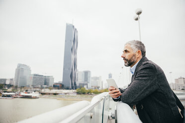 Österreich, Wien, Geschäftsmann mit Smartphone steht auf der Reichsbrücke und schaut in die Ferne - AIF000217