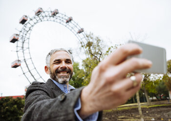 Österreich, Wien, Porträt eines lächelnden Geschäftsmannes, der ein Selfie im Prater macht - AIF000224