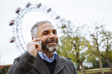 Österreich, Wien, Porträt eines lächelnden Geschäftsmannes, der mit einem Smartphone im Prater telefoniert - AIF000226