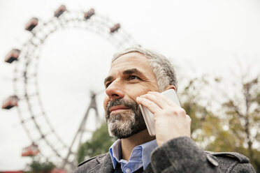 Österreich, Wien, Porträt eines lächelnden Geschäftsmannes, der mit einem Smartphone im Prater telefoniert - AIF000228