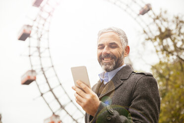 Österreich, Wien, Porträt eines lächelnden Geschäftsmannes mit Blick auf sein Smartphone im Prater - AIF000230