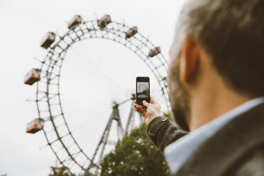 Österreich, Wien, Geschäftsmann fotografiert Riesenrad mit seinem Smartphone im Prater - AIF000233